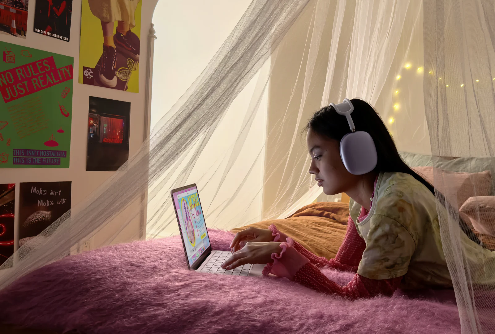 A girl using the MacBook Neo and wearing AirPods Max on her bed working