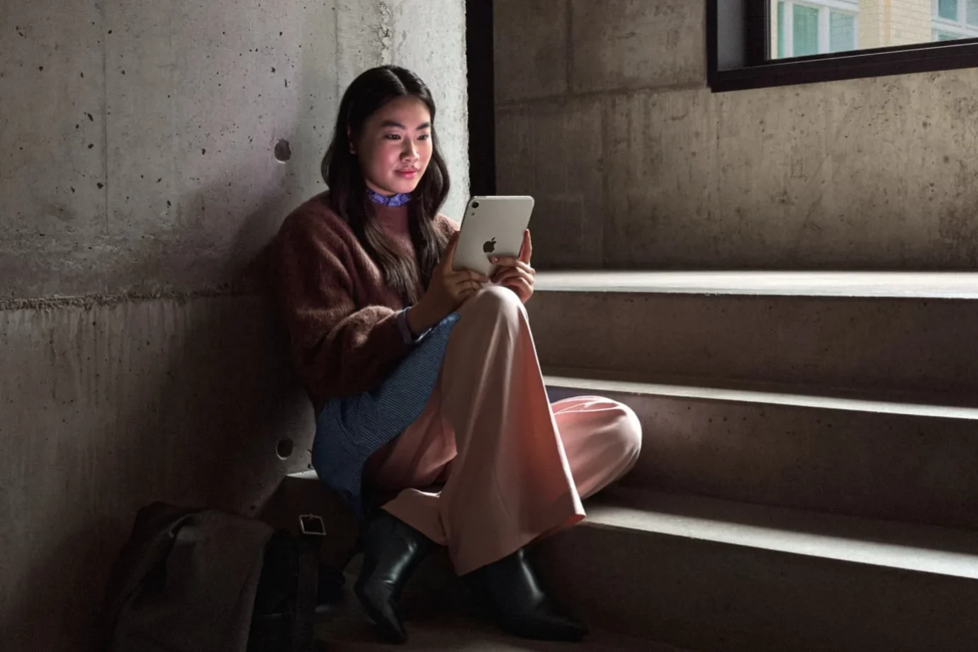 A girl sitting on stairs holding the iPad mini 8
